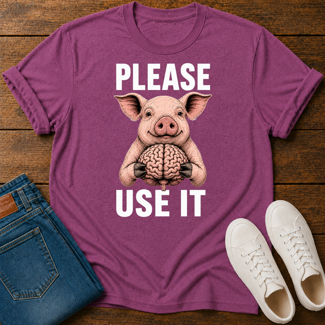 Pink T-Shirt with a graphic image of a cartoon pig holding a brain with text 'please use it' on a wooden board with jeans and sneakers