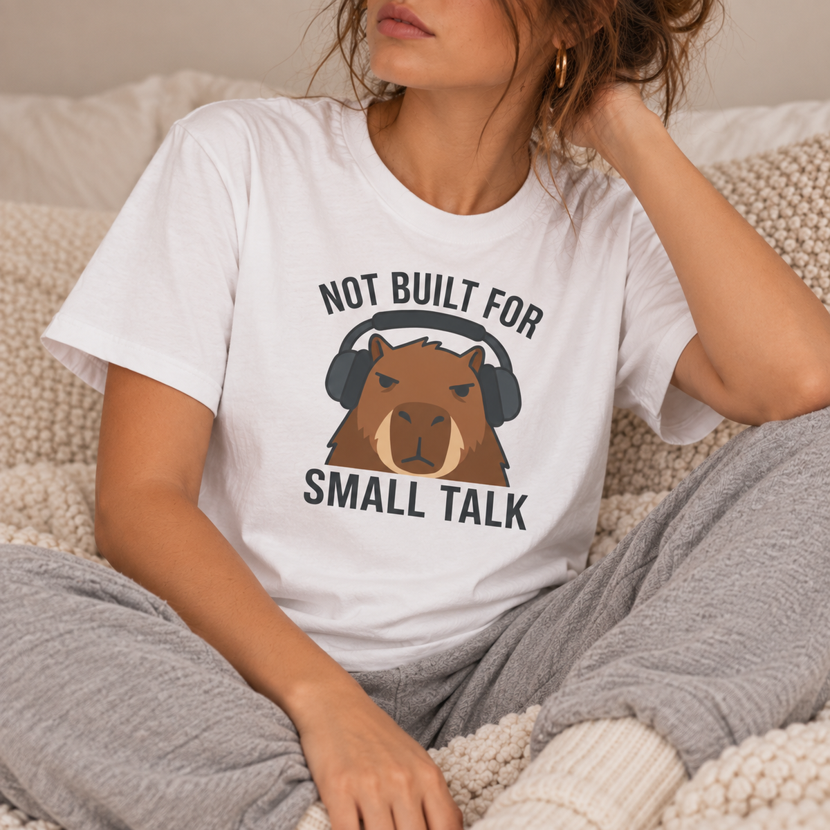 woman relaxing wearing a white t-shirt with capybara graphic and text 'not built for small talk'