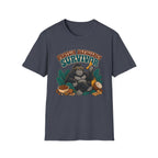 A blue short-sleeve crewneck t-shirt featuring a graphic of a gorilla wearing sunglasses and holding a banana, surrounded by text that reads 'PROTEIN DEFICITY SURVIVOR' and tropical elements like leaves, a coconut, and nuts.