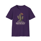 Purple short-sleeve crewneck t-shirt featuring a graphic of a cactus with a flower and the text 'I'D RATHER BE DIFFICULT THAN EASY TO USE' printed on the front, displayed against a solid white background.