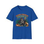 A royal blue short-sleeve crewneck t-shirt featuring a graphic of a gorilla wearing sunglasses and holding a banana, surrounded by text that reads 'PROTEIN DEFICITY SURVIVOR' and tropical elements like leaves, a coconut, and nuts.