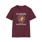 A maroon short-sleeve crewneck t-shirt with a graphic of a hamster in a running wheel and the text 'STILL PROCESSING THE LAST RIDICULOUS STATEMENT' on a plain white background.