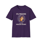A purple short-sleeve crewneck t-shirt featuring a graphic of a cartoon cat inside a running wheel with the text 'STILL PROCESSING THE LAST RIDICULOUS STATEMENT' printed on the front, set against a plain white background.