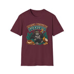 A maroon short-sleeve crewneck t-shirt featuring a graphic of a gorilla wearing sunglasses and holding a banana, surrounded by tropical leaves, nuts, and a bowl, with the text 'PROTEIN DEFICITY SURVIVOR' above it.
