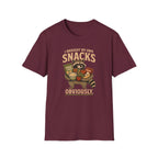 A maroon short-sleeve crewneck t-shirt featuring a vintage-style graphic of a raccoon holding a basket of snacks with the text 'I BROUGHT MY OWN SNACKS OBVIOUSLY.' printed on the front.
