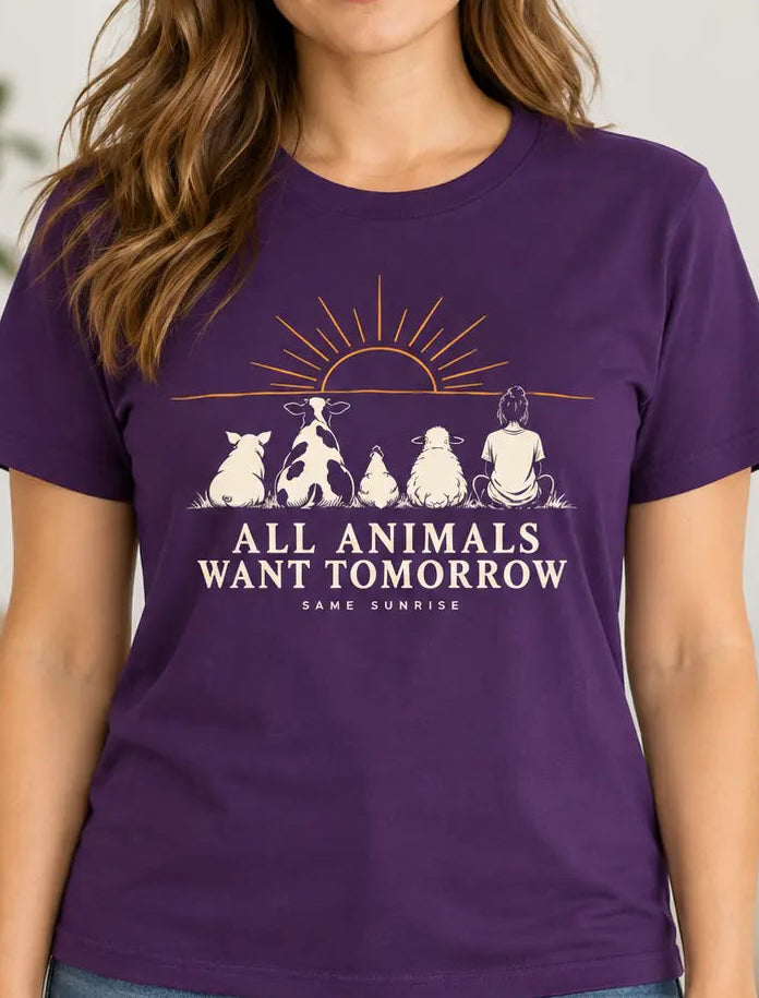 Woman wearing a purple graphic T-shirt featuring a pig, cow, chicken, sheep and person sitting beneath a sunrise with the words “All Animals Want Tomorrow” and “Same Sunrise.”