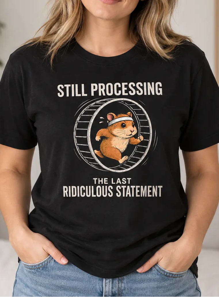 A woman wearing a black graphic t-shirt with a hamster illustration and the text 'STILL PROCESSING THE LAST RIDICULOUS STATEMENT' in a cozy indoor setting.