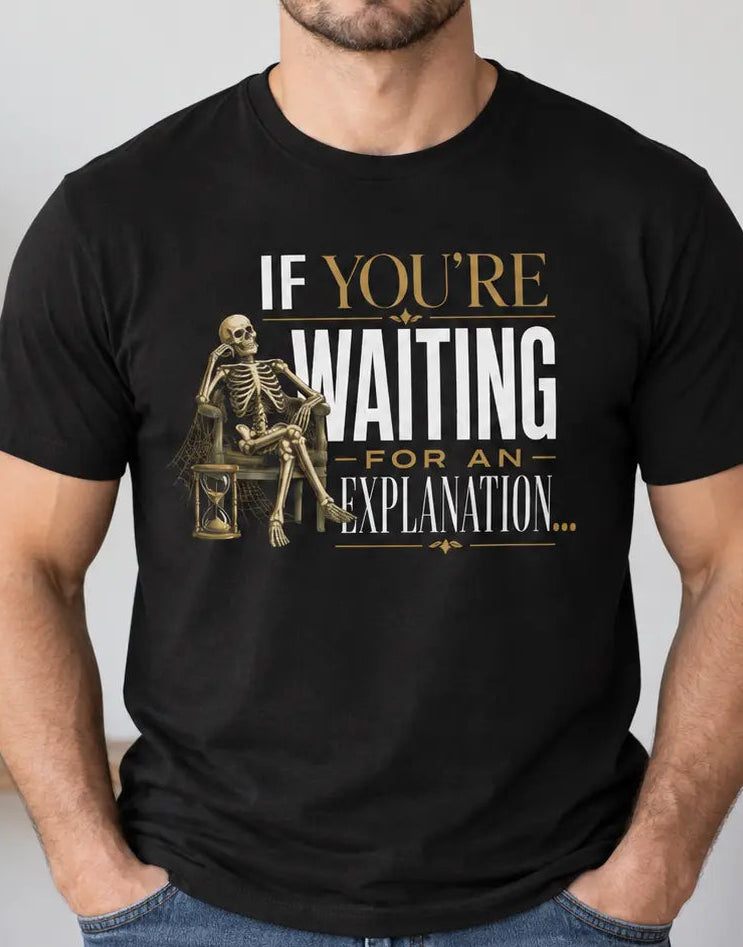 A man wearing a black graphic t-shirt with a gold and white skeleton design and the text 'IF YOU'RE WAITING FOR AN EXPLANATION.