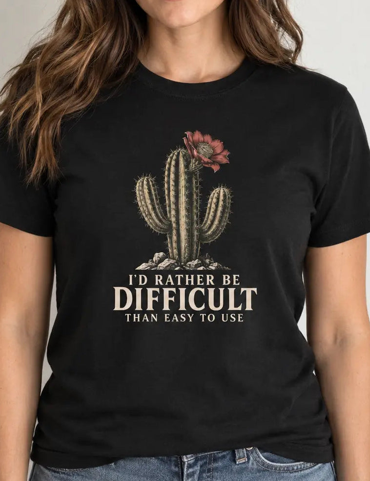 woman wearing a black short-sleeve crewneck t-shirt featuring a graphic of a cactus with a flower and the text 'I'D RATHER BE DIFFICULT THAN EASY TO USE' printed on the front, displayed against a solid white background.