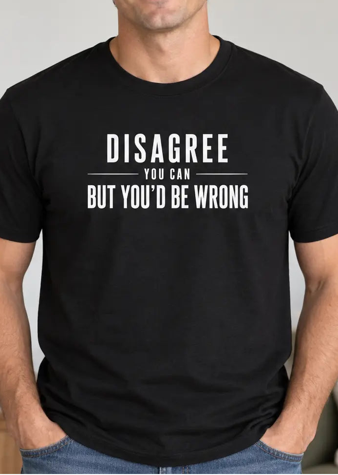 A man wearing a black crewneck t-shirt with white text that reads 'DISAGREE YOU CAN BUT YOU'D BE WRONG', standing in a brightly lit living room.