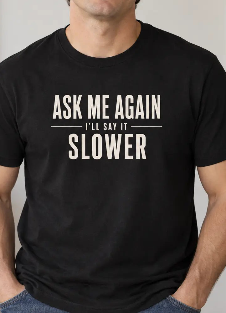 A man wearing a black t-shirt with the text 'ASK ME AGAIN I'LL SAY IT SLOWER' in white, standing in a brightly lit indoor setting.