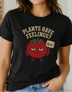 woman wearing a Black t-shirt with text "plants have feelings" and a tomato holding a sign 'bro!'