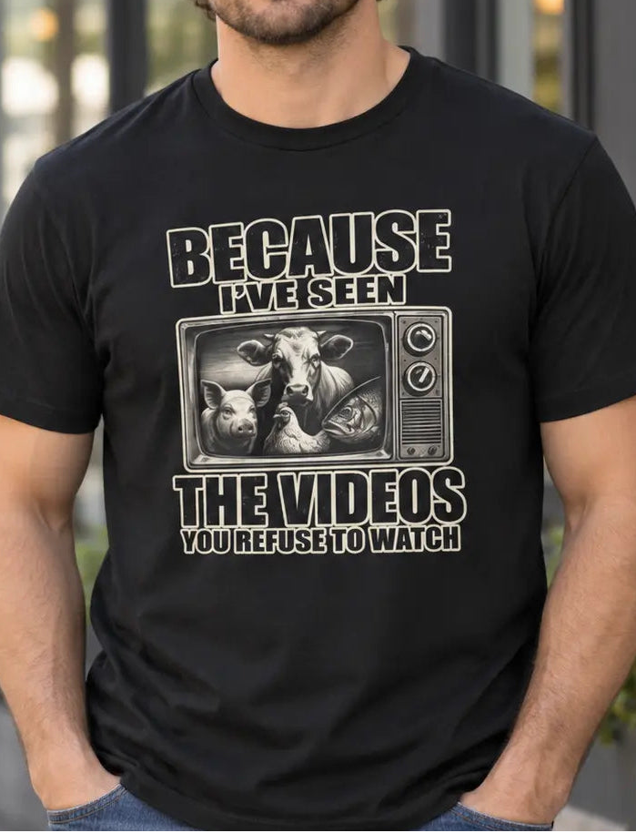 A man wearing a black graphic t-shirt with a humorous bull riding meme and the text 'BECAUSE I'VE SEEN THE VIDEOS YOU REFUSE TO WATCH', standing in front of a coffee shop storefront.