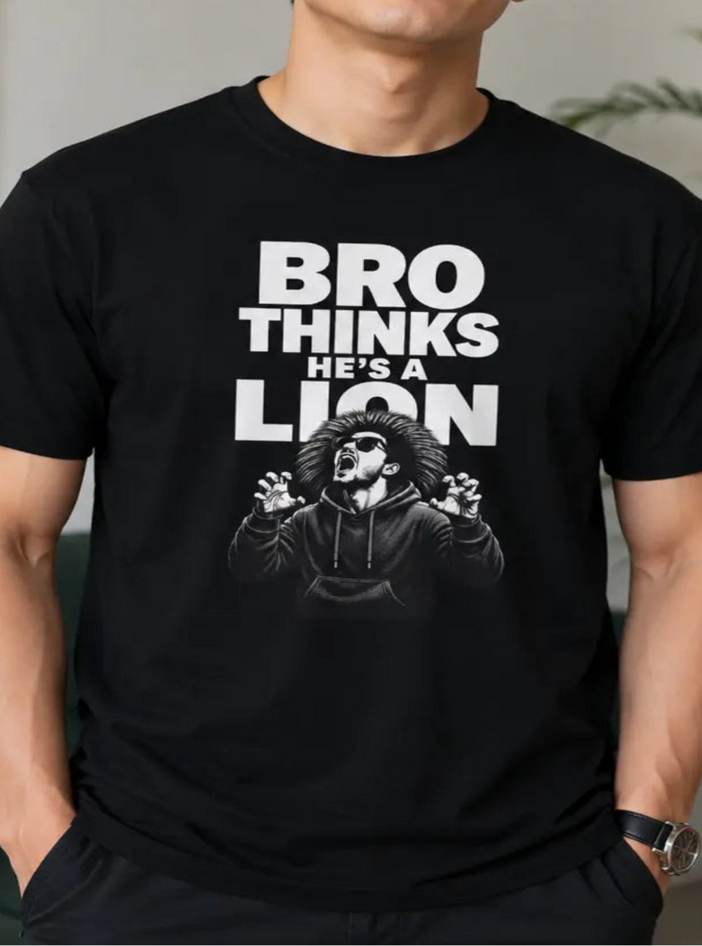 A man wearing a black vegan graphic t-shirt with the text 'BRO THINKS HE'S A LION' and a lion illustration, standing in a modern living room setting.