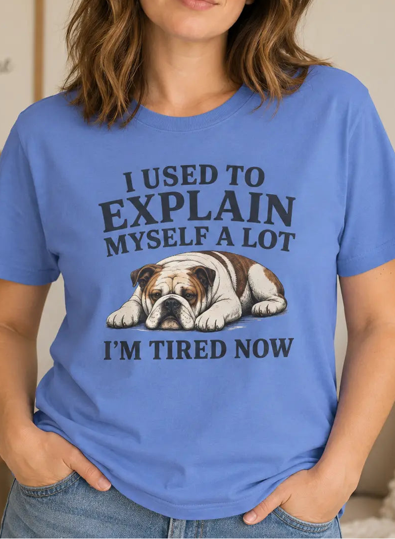 A woman wearing a blue graphic t-shirt with a bulldog illustration and the text 'I USED TO EXPLAIN MYSELF A LOT I'M TIRED NOW'.