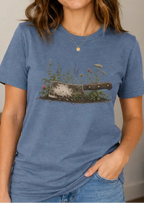 Woman wearing a blue t-shirt with image of a cleaver buried in the ground and flowers growing around it.