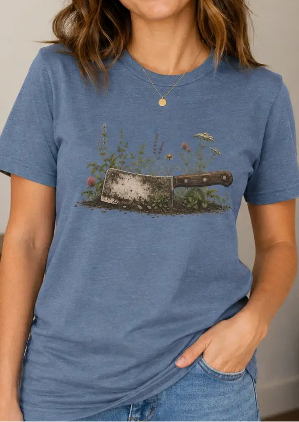 Woman wearing a blue t-shirt with image of a cleaver buried in the ground and flowers growing around it.