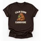 A dark brown short-sleeve t-shirt with a graphic of a capybara eating green leaves, surrounded by the text 'CALM DOWN CARNIVORE' in cream lettering, displayed on a clean white background.