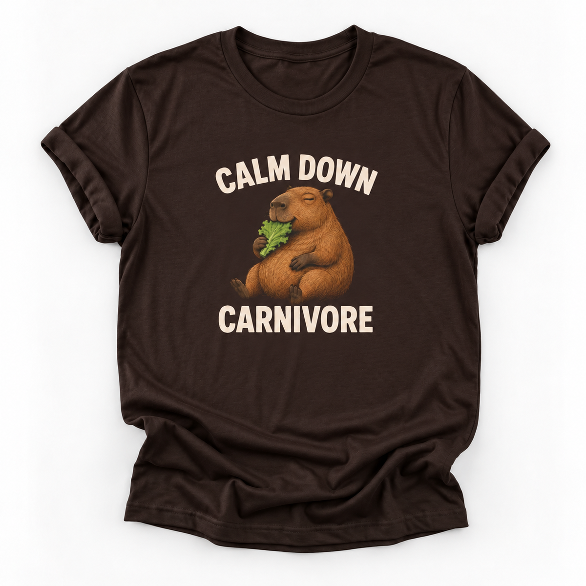 A dark brown short-sleeve t-shirt with a graphic of a capybara eating green leaves, surrounded by the text 'CALM DOWN CARNIVORE' in cream lettering, displayed on a clean white background.