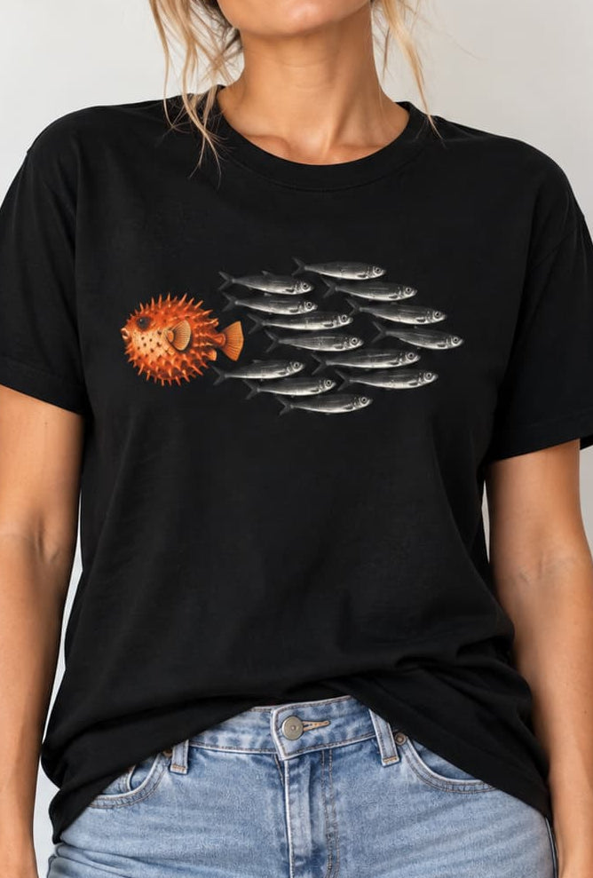 woman wearing a black Minimal graphic design featuring a bold orange pufferfish swimming in the opposite direction of a school of black sardines on a plain background.