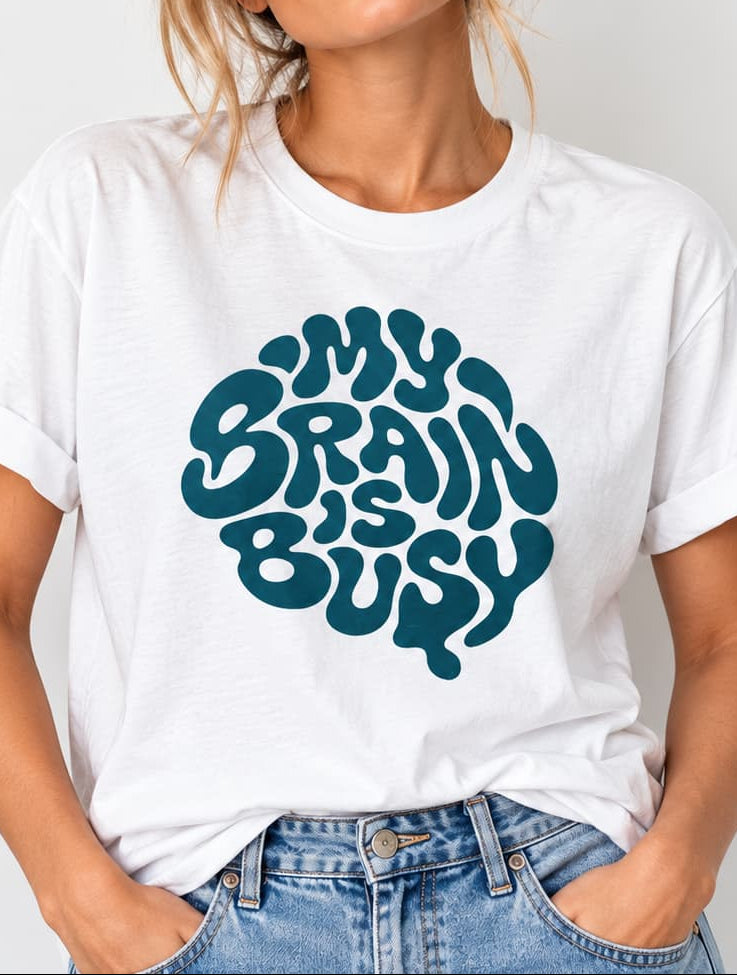 woman wearing a white Retro teal graphic design with the words “My Brain Is Busy” shaped into the outline of a human brain on a plain background.