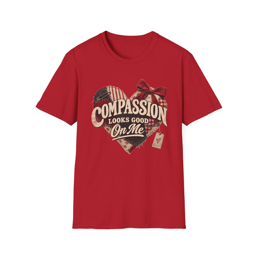 A red short-sleeve crewneck t-shirt featuring a distressed graphic on the front. The graphic shows a heart made of American flag and plaid patterns with a red bow, and the text 'COMPASSION LOOKS GOOD On Me' in a vintage cream font.