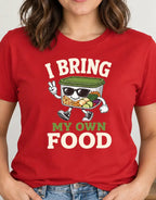 A woman wearing a red graphic t-shirt with a cartoon canned food character and the text 'I BRING MY OWN FOOD'.