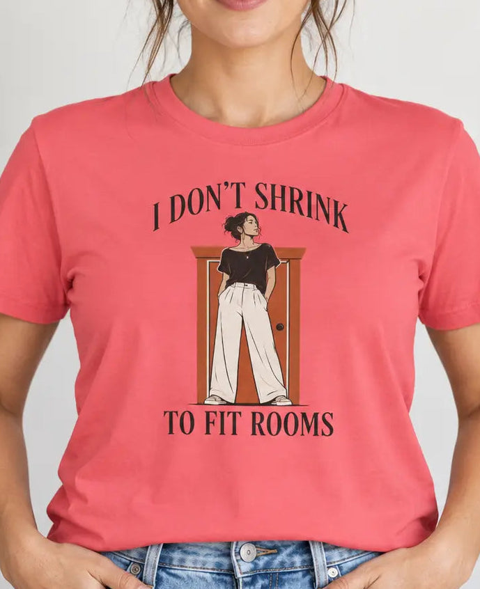 Woman wearing a coral pink shirt with graphic of a tall woman and text 'i don't shrink to fit rooms'
