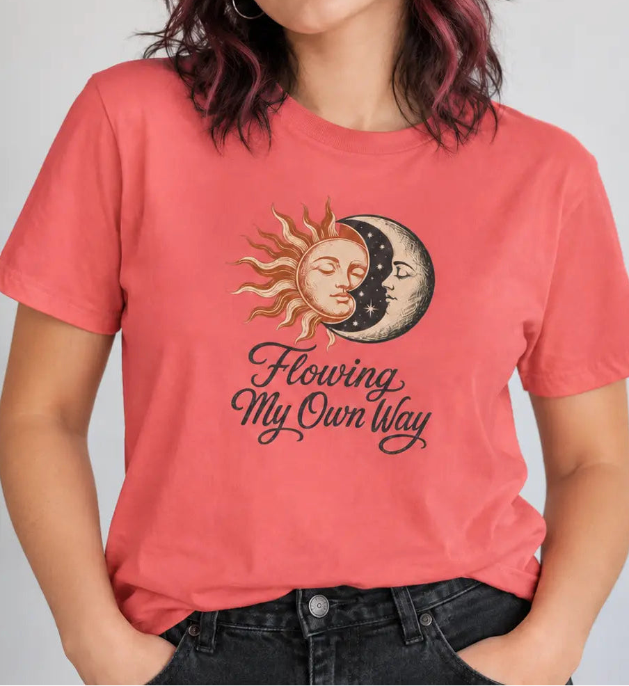 A woman wearing a coral pink graphic t-shirt with a sun and moon design and the text 'Flowing My Own Way'.