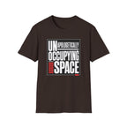 A dark brown short-sleeve t-shirt with a graphic print on the front reading 'UNAPOLOGETICALLY OCCUPYING SPACE' in white and red text inside a thin black rectangular border, shown on a plain white background.
