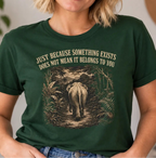 A woman wearing a dark green graphic t-shirt with a vintage-style elephant print and the text 'JUST BECAUSE SOMETHING EXISTS DOES NOT MEAN IT BELONGS TO YOU'.