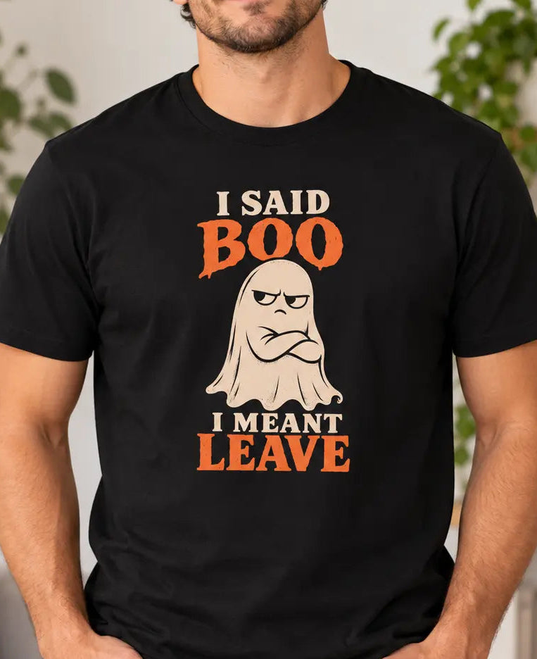 Man wearing a black graphic T-shirt featuring a grumpy cream ghost with crossed arms and the words “I Said Boo I Meant Leave” in cream and orange lettering.