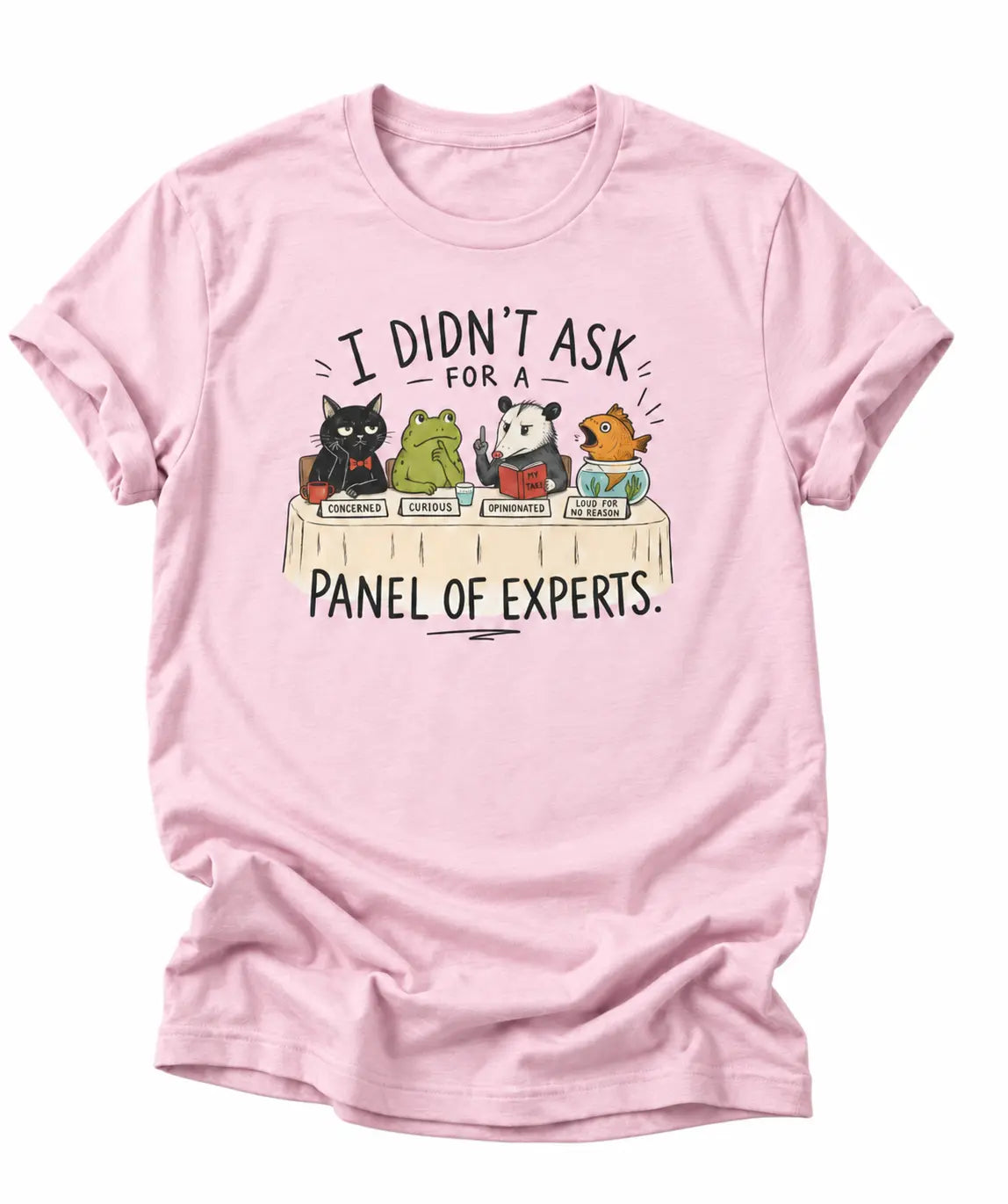 A light pink short-sleeve crewneck t-shirt featuring a cartoon graphic of five animals (a cat, frog, panda, and two birds) sitting on books, with the text 'I DIDN'T ASK FOR A PANEL OF EXPERTS.' printed above and below.