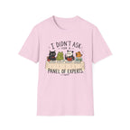 A light pink short-sleeve crewneck t-shirt featuring a cartoon graphic of five animals (a cat, frog, panda, and two birds) sitting on books, with the text 'I DIDN'T ASK FOR A PANEL OF EXPERTS.' printed above and below.