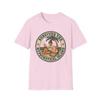 A light pink short-sleeve crewneck t-shirt featuring a circular retro-style graphic on the chest with the text 'SURVIVED THE HYPOTHETICAL ISLAND' and an illustration of a woman and child under a palm tree.