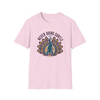 A light pink short-sleeve crewneck t-shirt featuring a graphic of a teal peacock with its tail fanned out, surrounded by the text 'NEVER DOING SUBTLE' in a dark arched font.