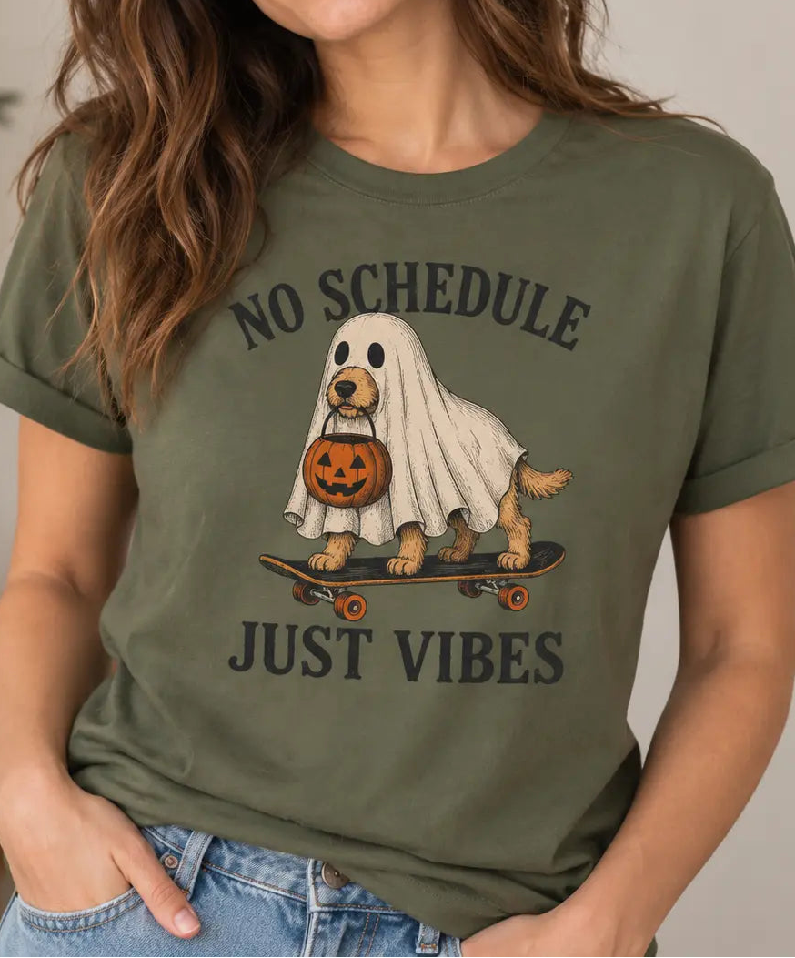 Woman wearing a military green colored t-shirt with halloween graphic and text 'no schedule just vibes'