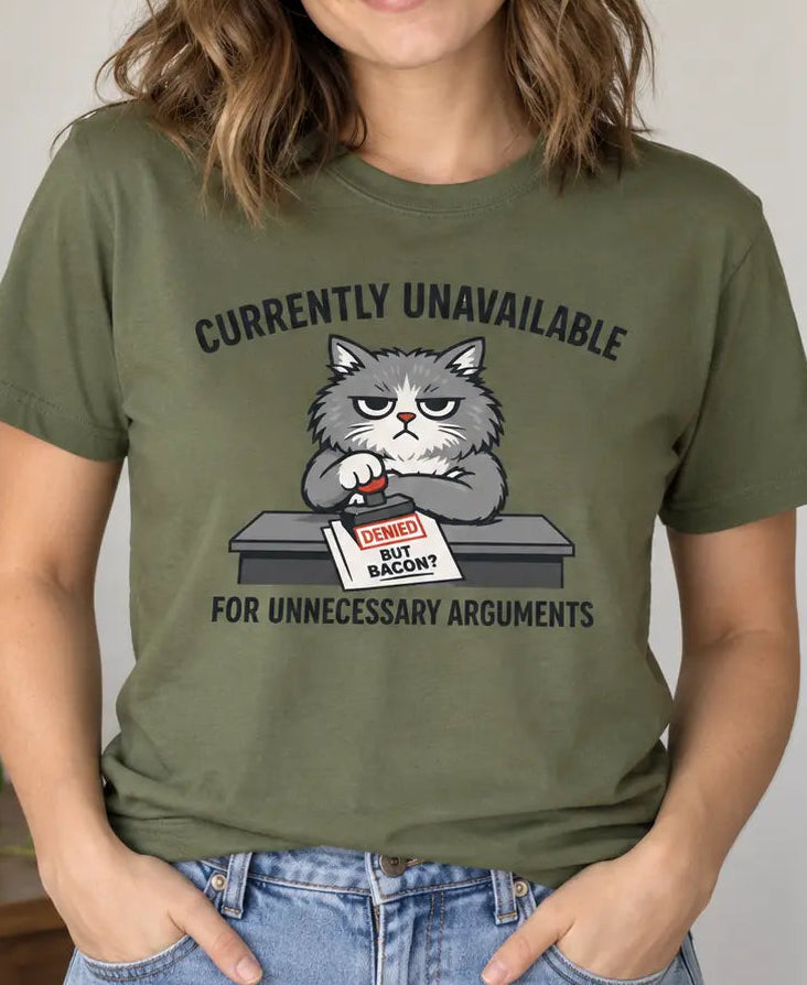 A woman wearing an olive green graphic t-shirt with a cartoon cat sitting at a desk and the text 'CURRENTLY UNAVAILABLE FOR UNNECESSARY ARGUMENTS'.