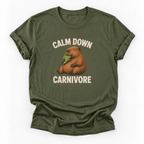 An olive green short-sleeve t-shirt with a graphic of a capybara holding green leaves, with the text 'CALM DOWN CARNIVORE' printed in beige above and below the illustration.
