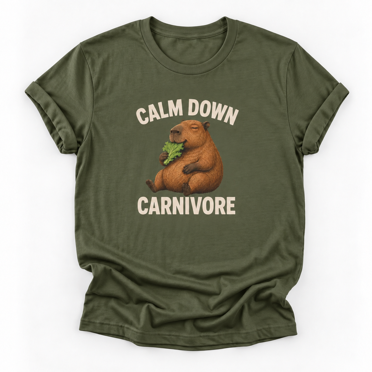 An olive green short-sleeve t-shirt with a graphic of a capybara holding green leaves, with the text 'CALM DOWN CARNIVORE' printed in beige above and below the illustration.