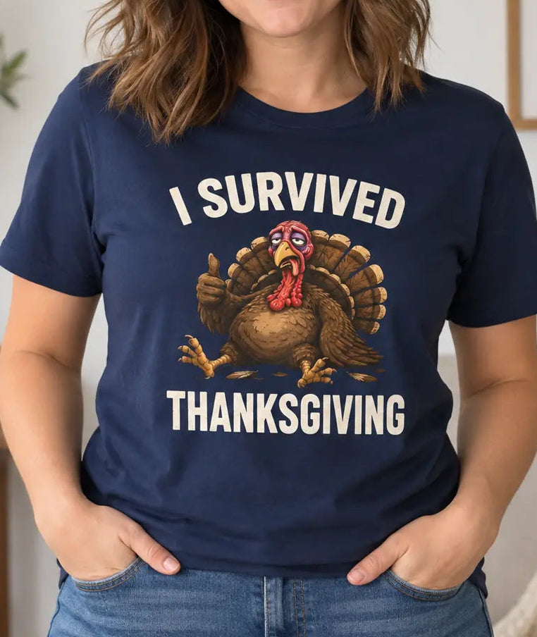 A woman wearing a navy blue graphic t-shirt with a turkey illustration and the text 'I SURVIVED THANKSGIVING' in white, standing in a cozy living room setting.