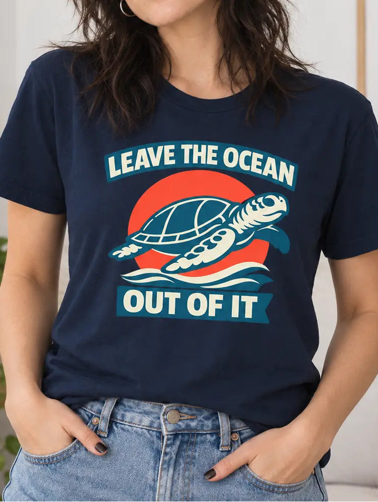 A woman wearing a navy blue graphic t-shirt with a turtle design and the text 'LEAVE THE OCEAN OUT OF IT', paired with light wash blue jeans in a bright, modern living room setting.