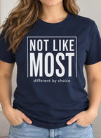 A woman wearing a navy blue graphic t-shirt with the text 'NOT LIKE MOST different by choice' in white, standing in a brightly lit living room.