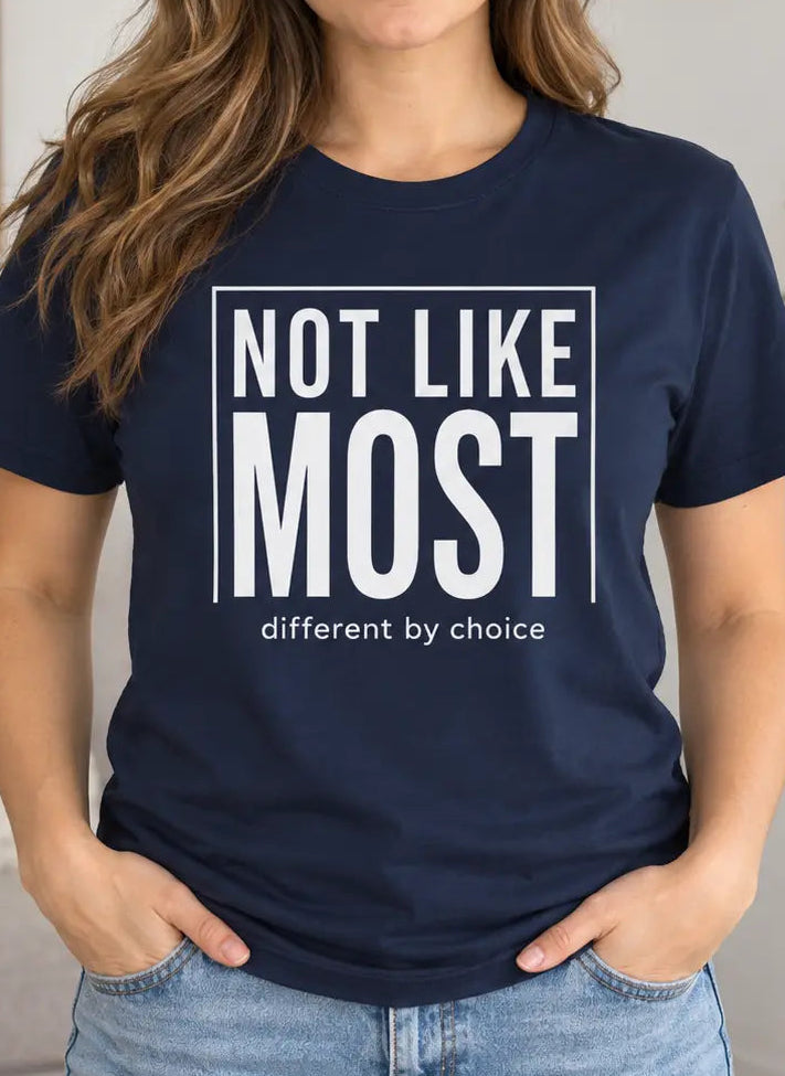 A woman wearing a navy blue graphic t-shirt with the text 'NOT LIKE MOST different by choice' in white, standing in a brightly lit living room.