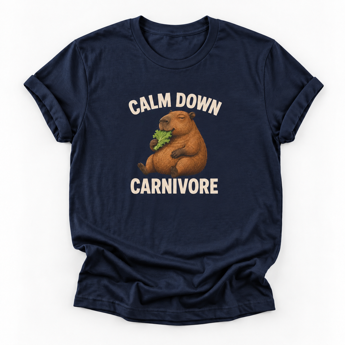 A navy blue short-sleeve t-shirt with a graphic of a capybara eating green leaves, surrounded by the text 'CALM DOWN CARNIVORE' in cream lettering, shown on a plain white background.