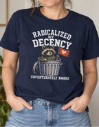 A woman wearing a navy blue graphic t-shirt with a cartoon sloth in a trash can and the text 'RADICALIZED BY DECENCY UNFORTUNATELY AWARE'. She is standing in a brightly lit room with a wooden dresser, a green plant, and a framed print on the wall.