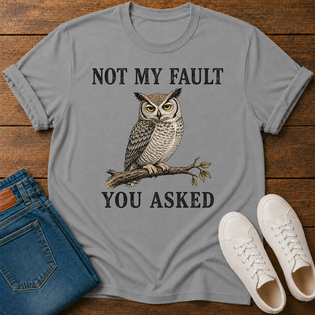 A heather gray graphic t-shirt featuring a owl illustration and the text 'NOT MY FAULT YOU ASKED', styled in a flat lay on a wooden background with blue jeans and white sneakers.