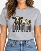 Woman wearing a Grey vegan t-shirt Black and cream graphic featuring a cow, pig and chicken emerging from vertical barcode lines above the words “Not A Product.”
