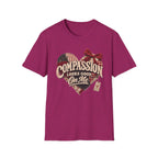 A heather magenta short-sleeve t-shirt with a graphic on the chest featuring a heart made of American flag and plaid patterns, a red bow, and the text 'COMPASSION LOOKS GOOD ON ME'.