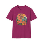 A heather magenta short-sleeve t-shirt with a retro-style graphic on the chest reading 'Not Born To Blend' in orange lettering, surrounded by a tropical sunset design with waves, flowers, and palm trees.